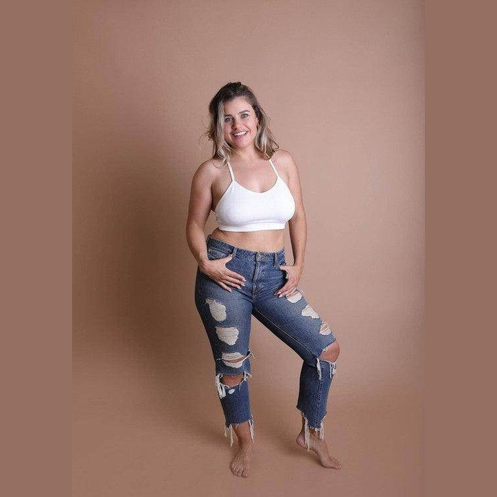 Plus size model wearing a white racerback bralette plus size with distressed jeans for a trendy look