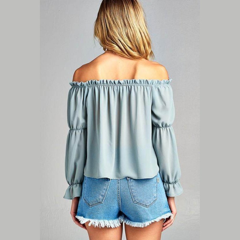 Back view of a women's ruffled front tie long sleeve blouse in blue styled with denim shorts