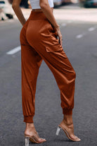 Women wearing rust-colored satin cargo joggers with side pockets and elastic cuffs
