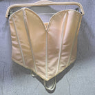 Sexy party club bustier top in light beige satin hanging on a wooden hanger against gray wall