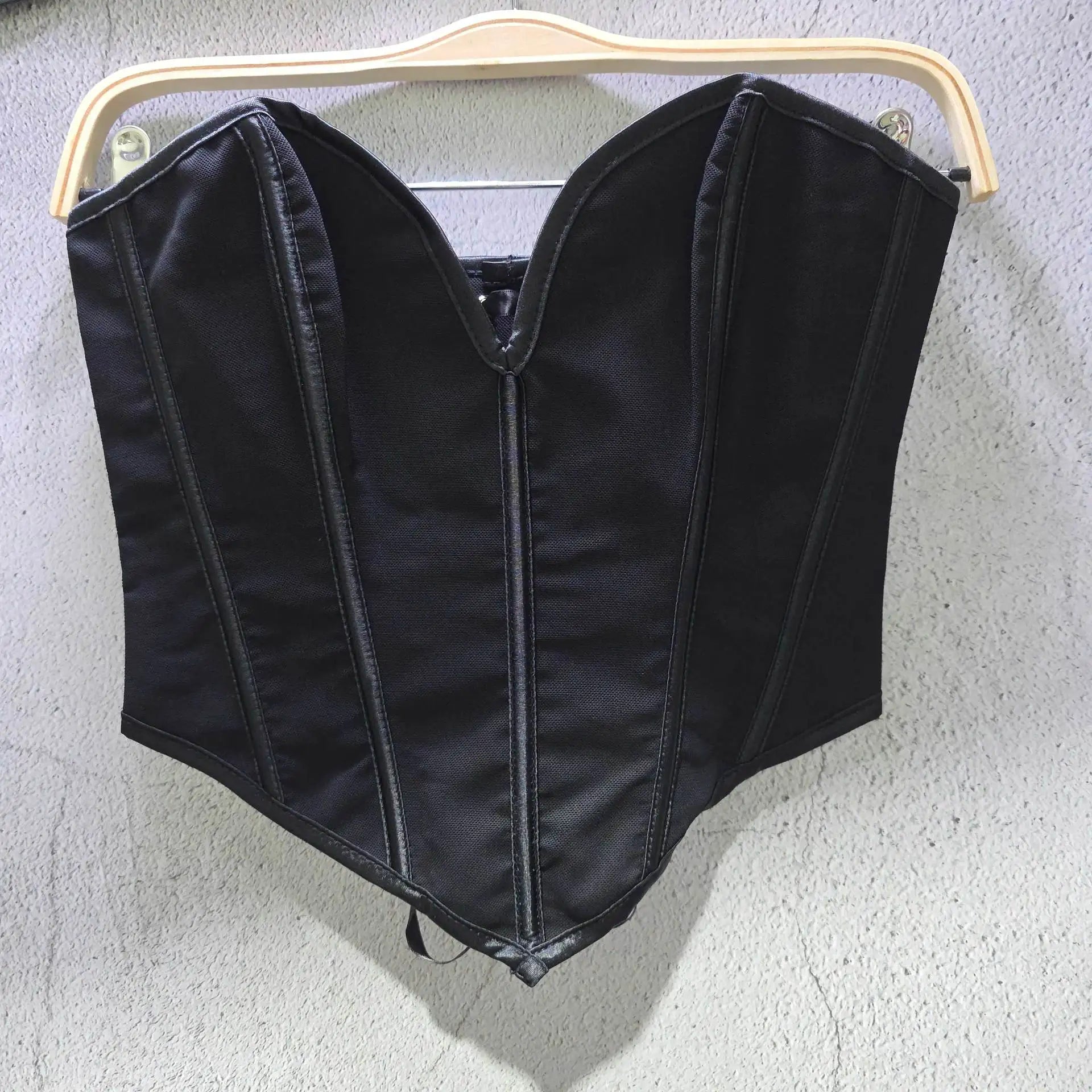 Black sexy party club bustier top hanging on wooden hanger against gray wall