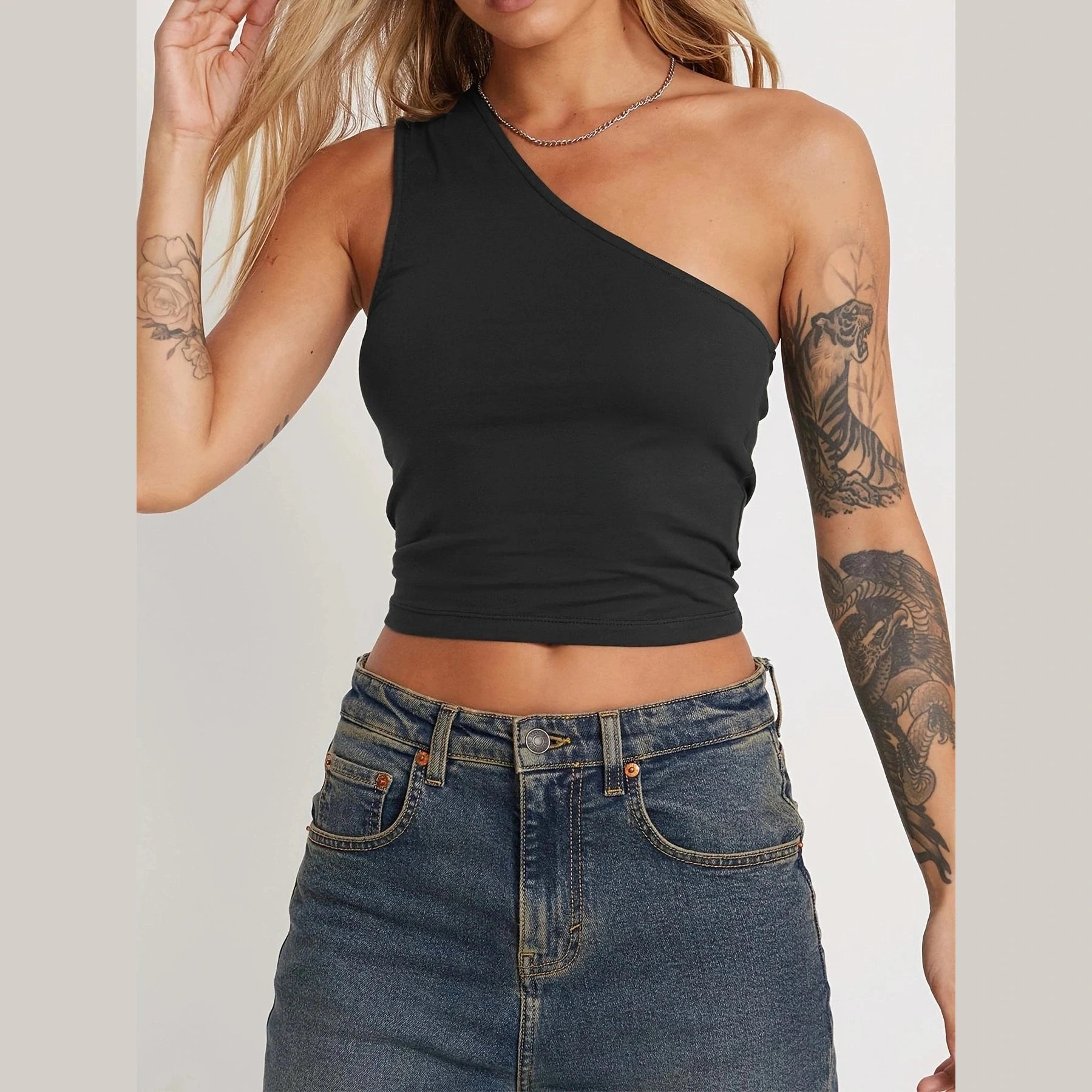 Black one shoulder crop top worn by woman with tattoos paired with denim jeans sexy vacation tops for women