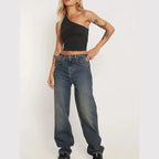 Woman wearing a black one-shoulder sexy vacation tops for women paired with relaxed fit jeans