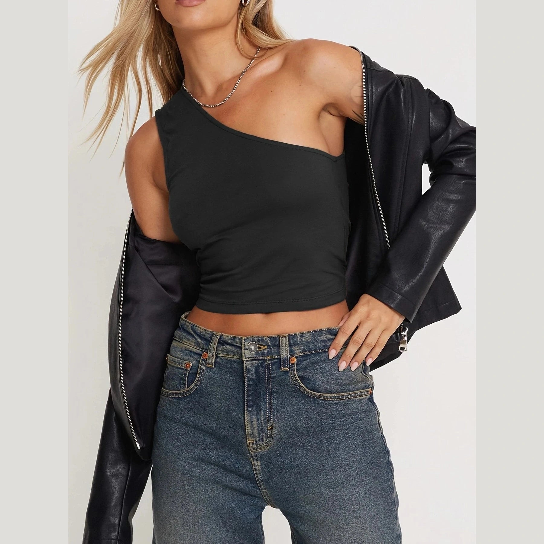Woman wearing black one-shoulder crop top and leather jacket showcasing sexy vacation tops for women