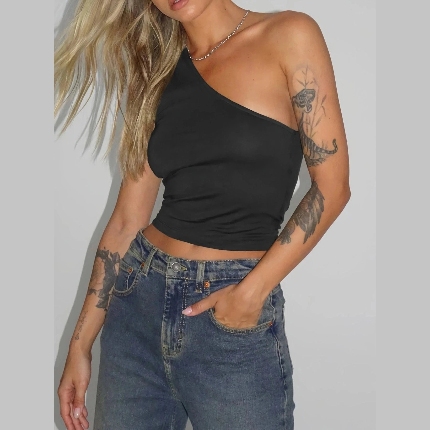 Black one-shoulder sexy vacation tops for women styled with high-waisted blue jeans and silver necklace