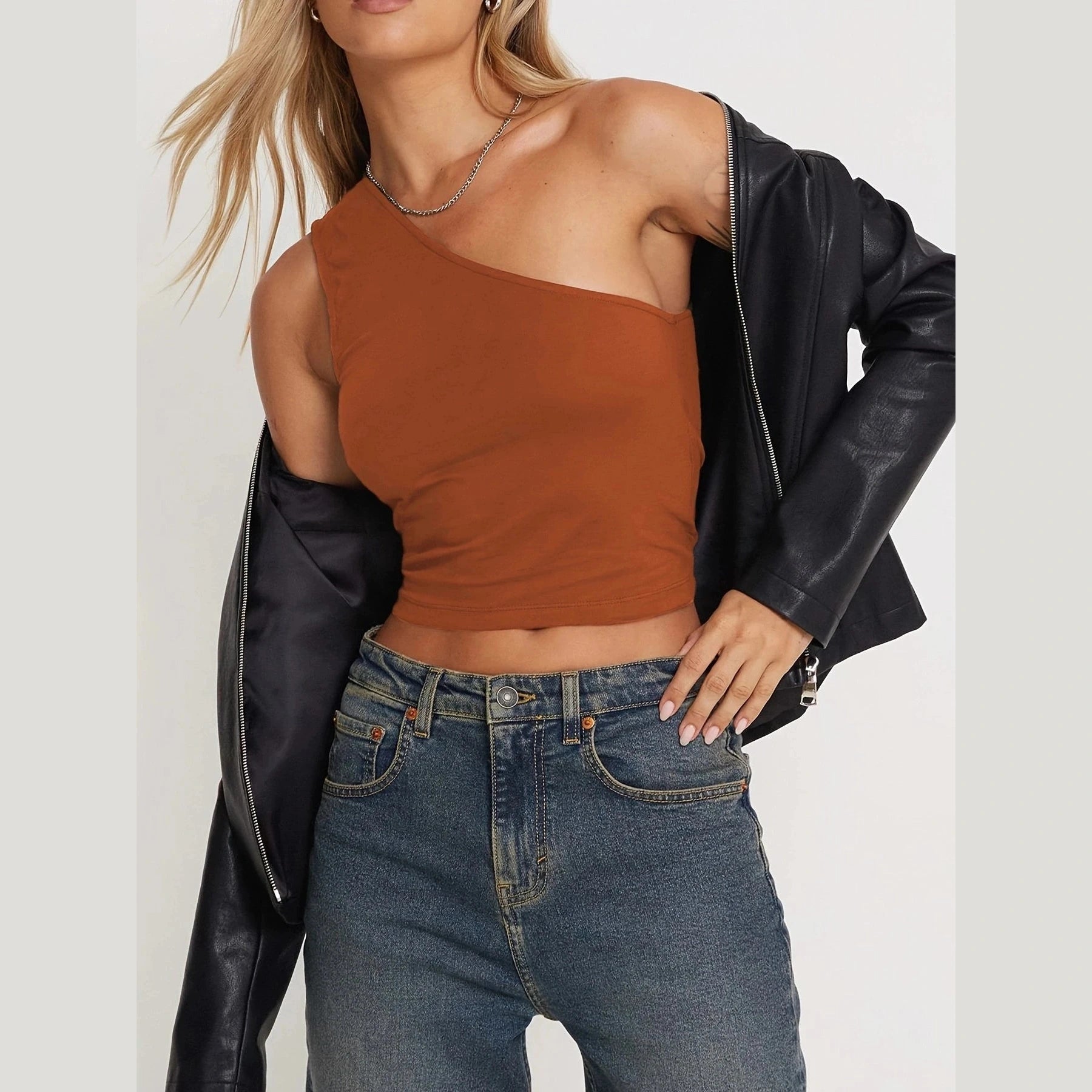 Woman wearing a brown one-shoulder crop top and denim jeans with a black leather jacket for sexy vacation tops for women