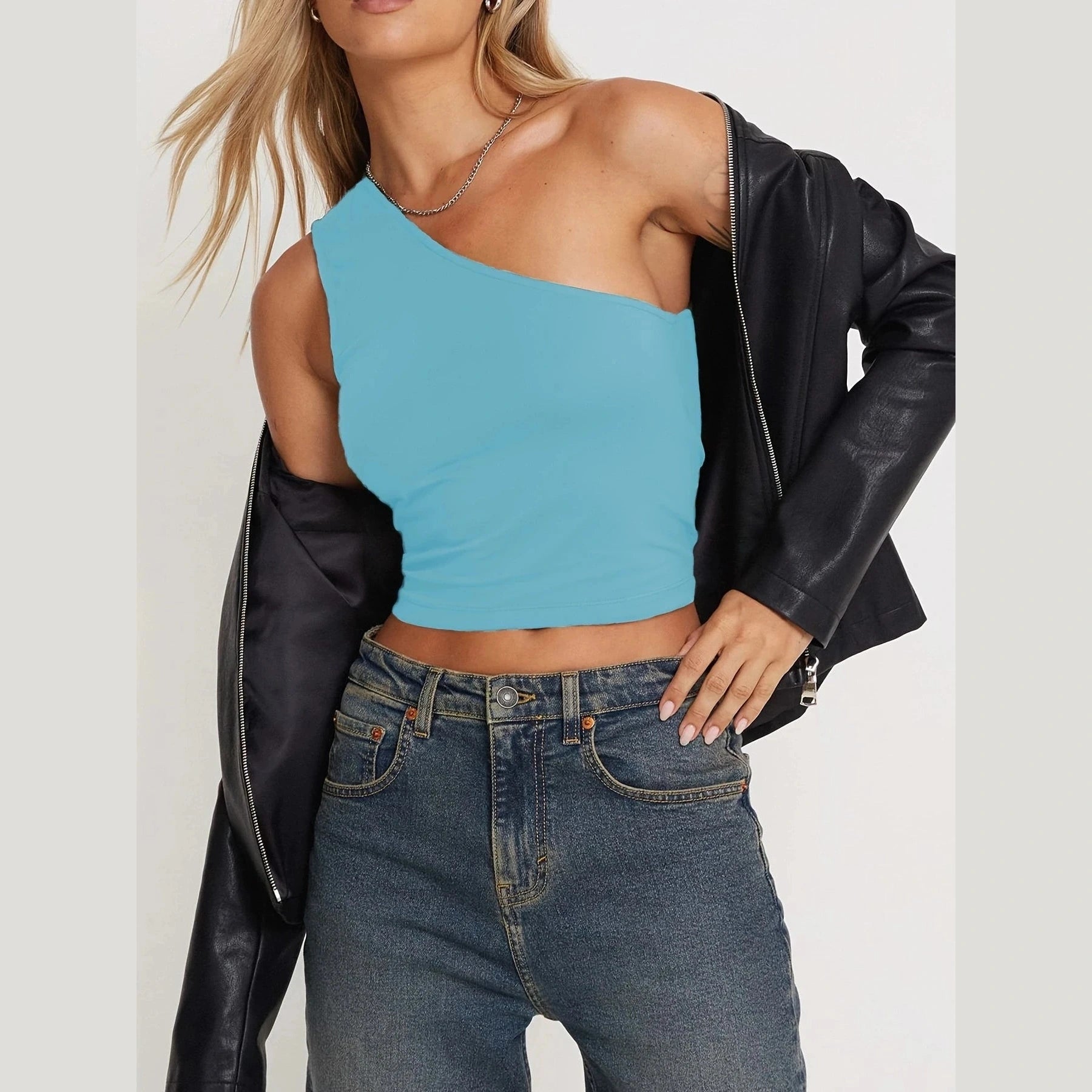Woman wearing a blue one-shoulder crop top paired with jeans and a black leather jacket sexy vacation tops for women