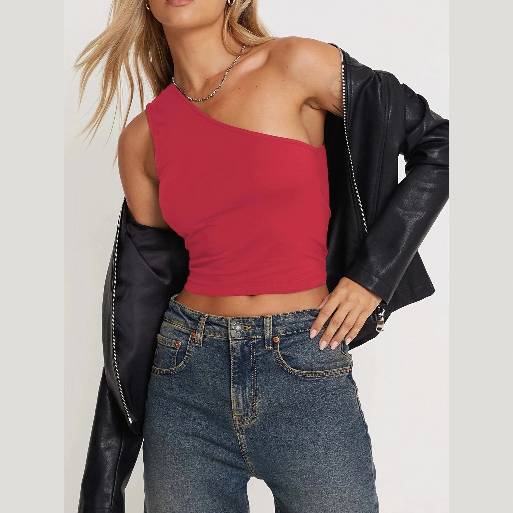 Woman wearing a red one-shoulder cropped top paired with jeans and a black leather jacket sexy vacation tops for women