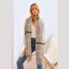 Stylish winter scarf for vacations in gray plaid pattern, worn by a model with jeans and a cream sweater
