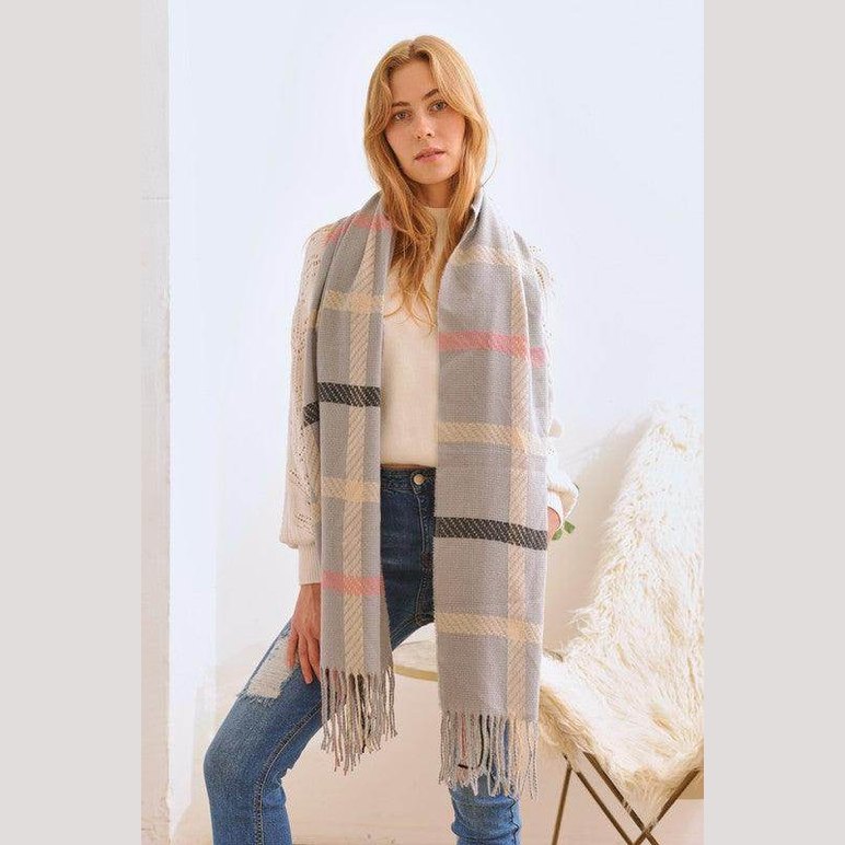 Stylish winter scarf for vacations in gray plaid pattern, worn by a model with jeans and a cream sweater