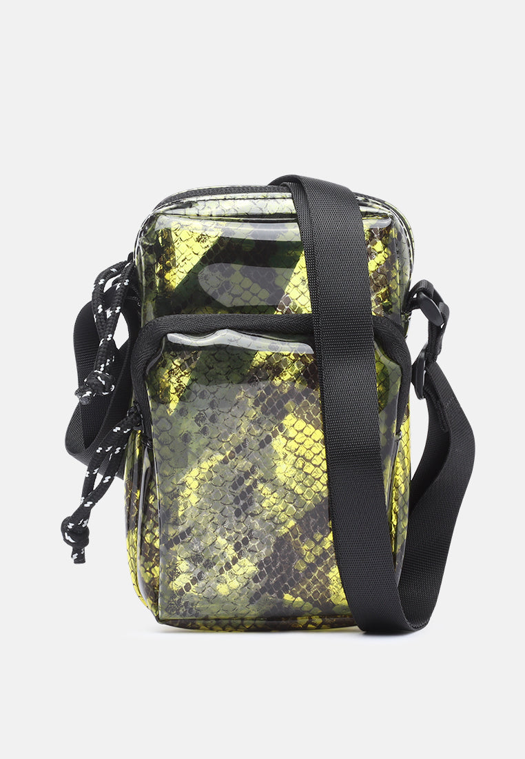 A small crossbody phone bag with a glossy black and yellow-green snakeskin pattern, featuring a black adjustable shoulder strap and a black chain detail on the side, set against a plain light gray background.