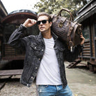 Man wearing sunglasses holding a textured travel weekender bag while posing outdoors in casual attire