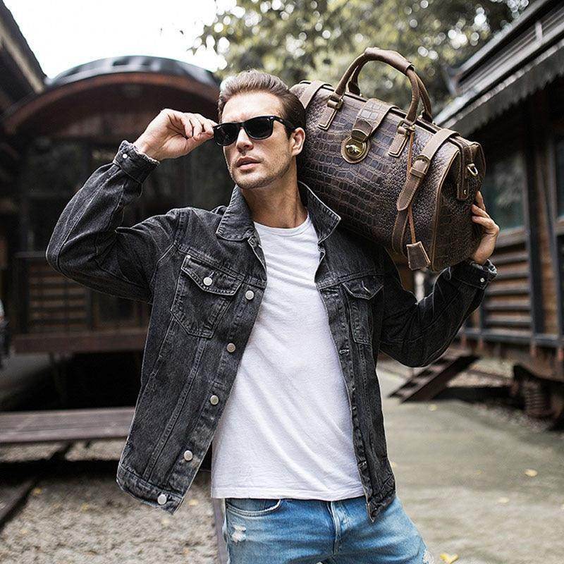 Man wearing sunglasses holding a textured travel weekender bag while posing outdoors in casual attire