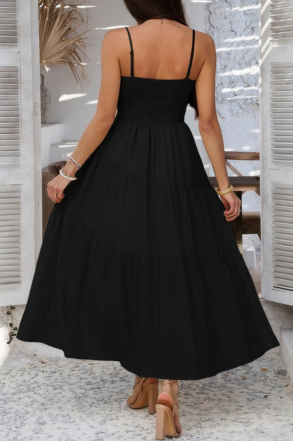 Back view of a black tiered cami vacation dress with adjustable straps and flowy design
