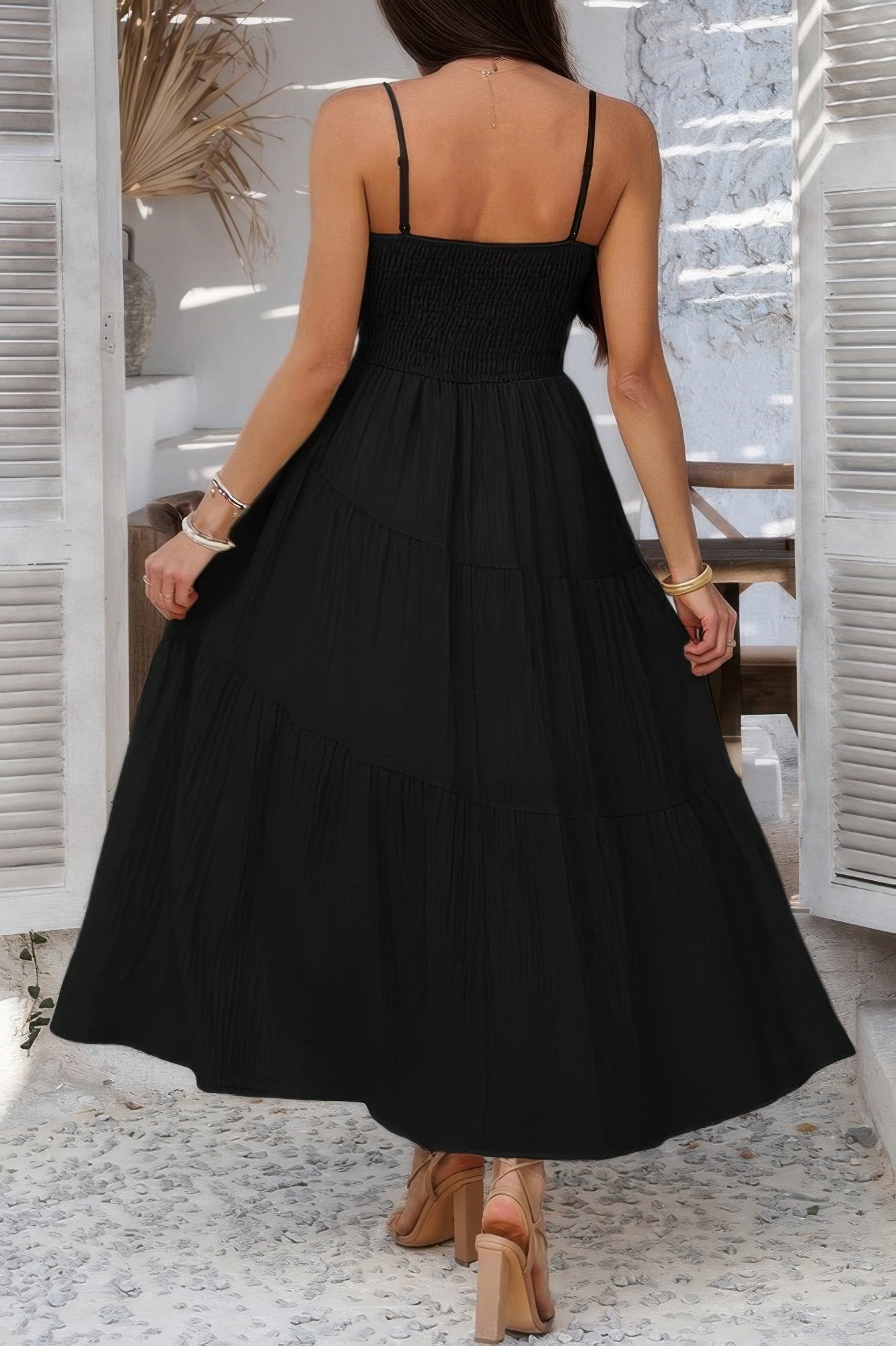 Back view of a black tiered cami vacation dress with adjustable straps and flowy design