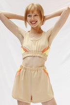 Woman wearing trendy retro activewear beige crop top and shorts with orange and yellow accents by Miss Sparkling