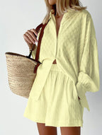 Woman wearing light yellow loose shirt and shorts vacation outfit for women holding a woven straw bag