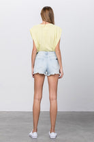 Back view of women's vacation style denim shorts paired with a light yellow top in a casual setting