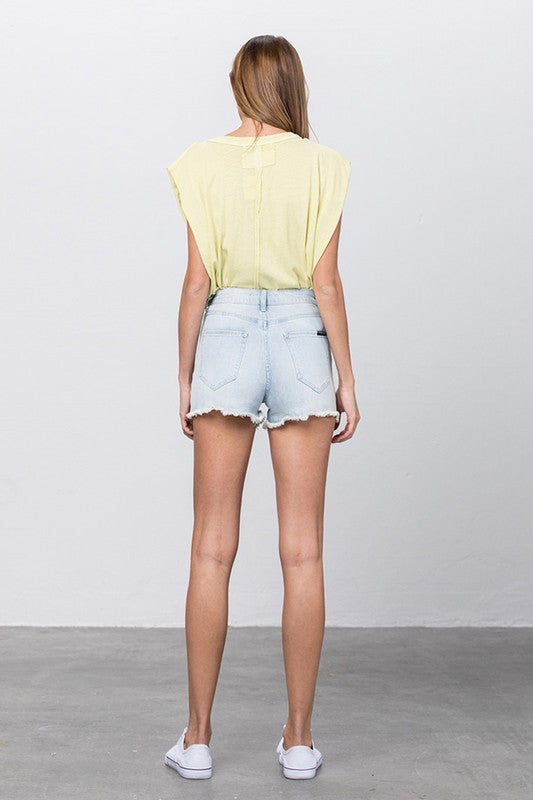 Back view of women's vacation style denim shorts paired with a light yellow top in a casual setting