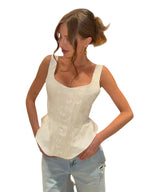 VacationGrabs white satin corset tank top with wide straps worn by a woman with light blue jeans in a modern lounge