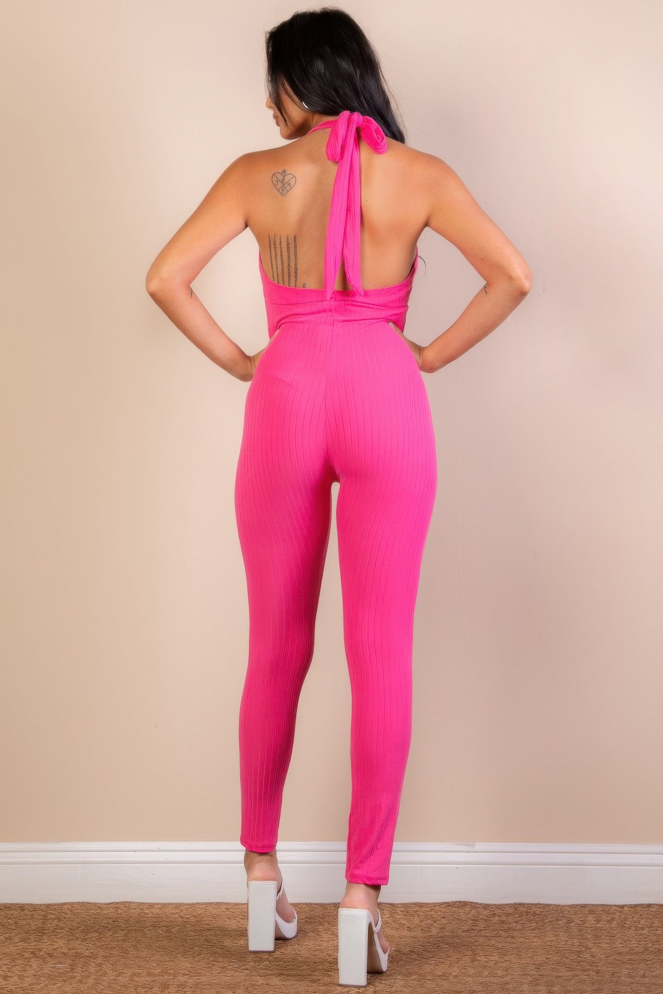 Back view of a pink ribbed bodycon jumpsuit for women with a halter neck and tie detailing