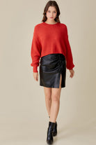 Woman wearing a Mustard Seed red knit sweater paired with a black leather ruched skirt trendy sweater tops for women
