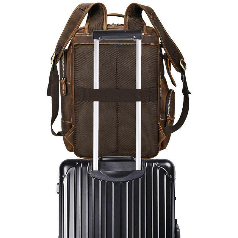 Vintage leather backpack with adjustable straps placed on top of a black suitcase