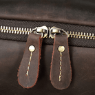 Close-up of a vintage leather backpack zipper with brass pulls and sturdy stitching for durability