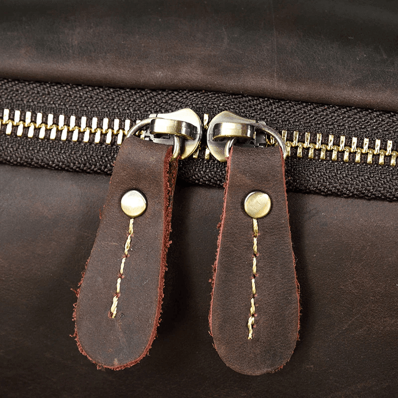 Close-up of a vintage leather backpack zipper with brass pulls and sturdy stitching for durability