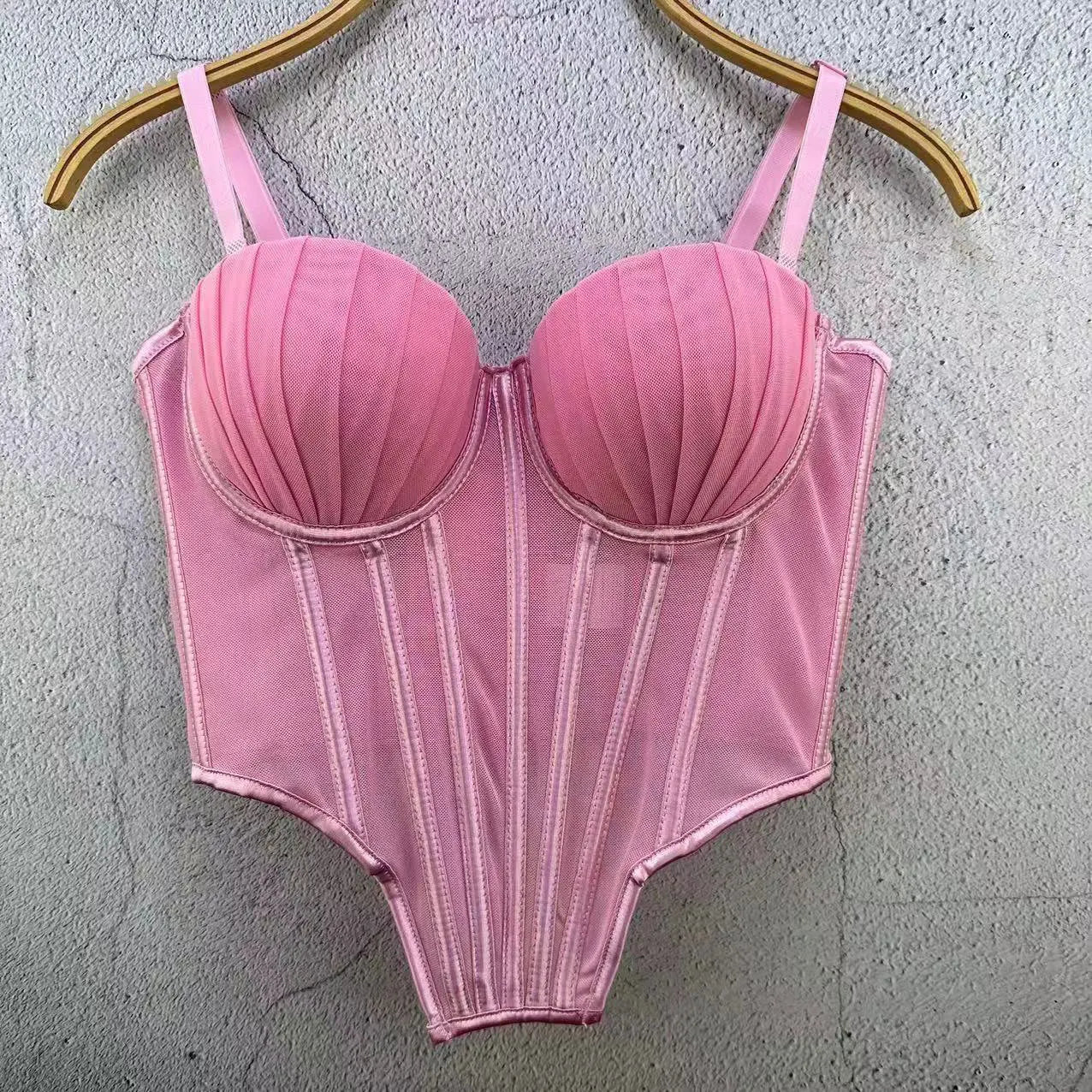 Pink sexy clubwear bustier shirt with structured cups and adjustable straps hanging on wooden hanger
