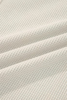 Close-up of a soft cream waffle knit henley top fabric showing texture and warmth