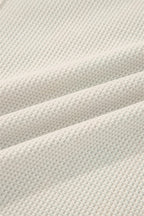 Close-up of a soft cream waffle knit henley top fabric showing texture and warmth