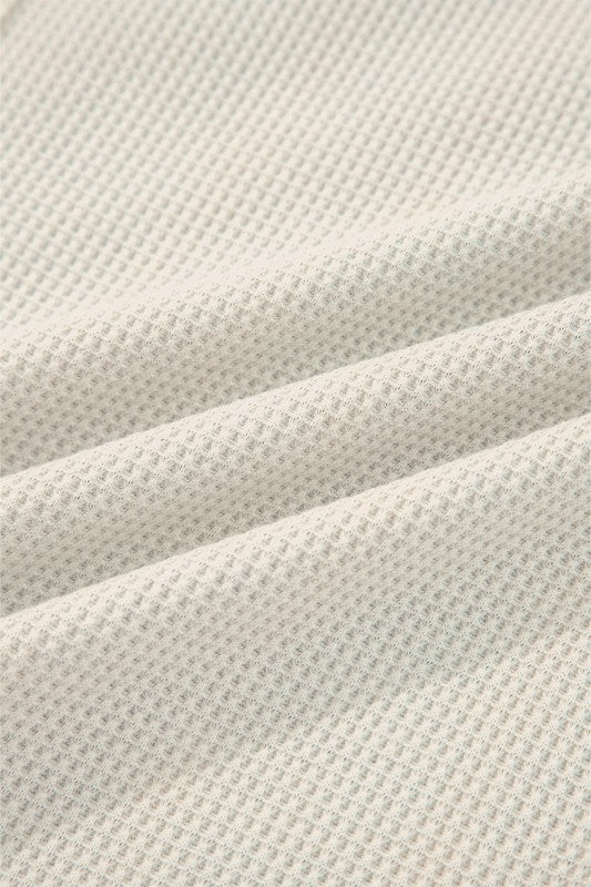 Close-up of a soft cream waffle knit henley top fabric showing texture and warmth