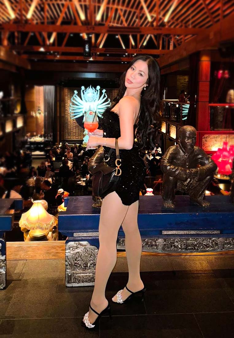 Stylish woman in black dress and women's high heel sandals holding a cocktail in an upscale restaurant
