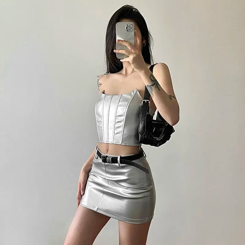 Woman wearing a womens metallic skirt and crop top set in silver holding a phone taking a mirror selfie