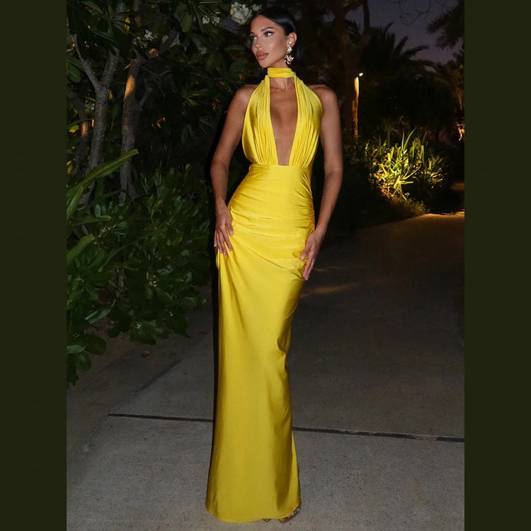 Woman wearing a yellow halter deep v neck maxi dress standing outdoors at night
