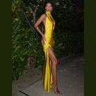 Woman wearing yellow halter deep v neck maxi dress with thigh slit and gold heels outdoors at night