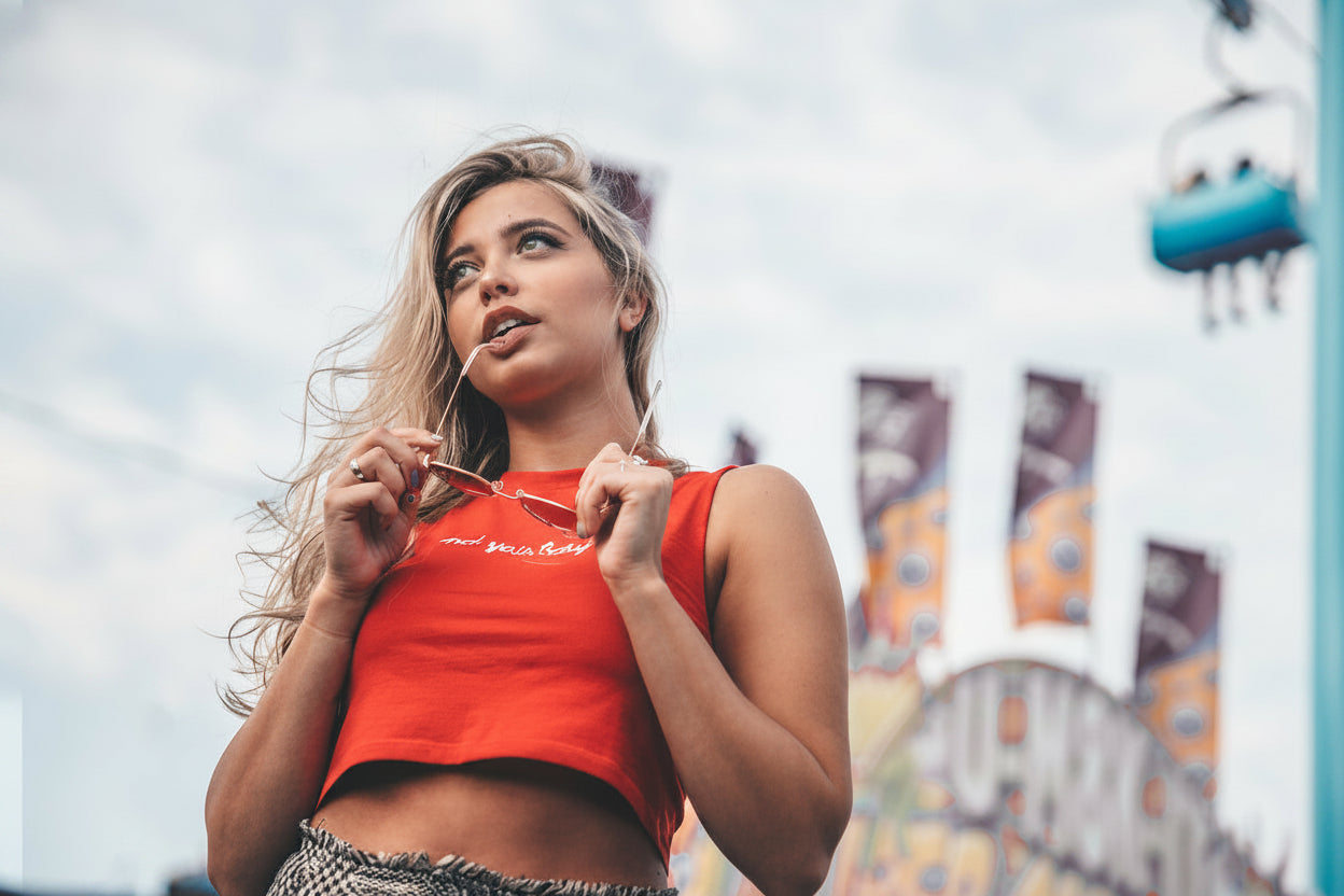 Woman in a red crop top standing in front of an amusement park with Ferris wheel in the background