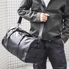 Black leather weekend bag with adjustable strap held by a person in a stylish outfit