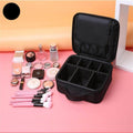 Portable makeup bag for trips in black, featuring multiple compartments and makeup tools arranged on a pink surface
