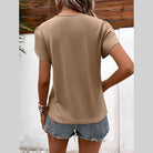 Back view of a women's casual v-neck vacation shirt in beige paired with denim shorts