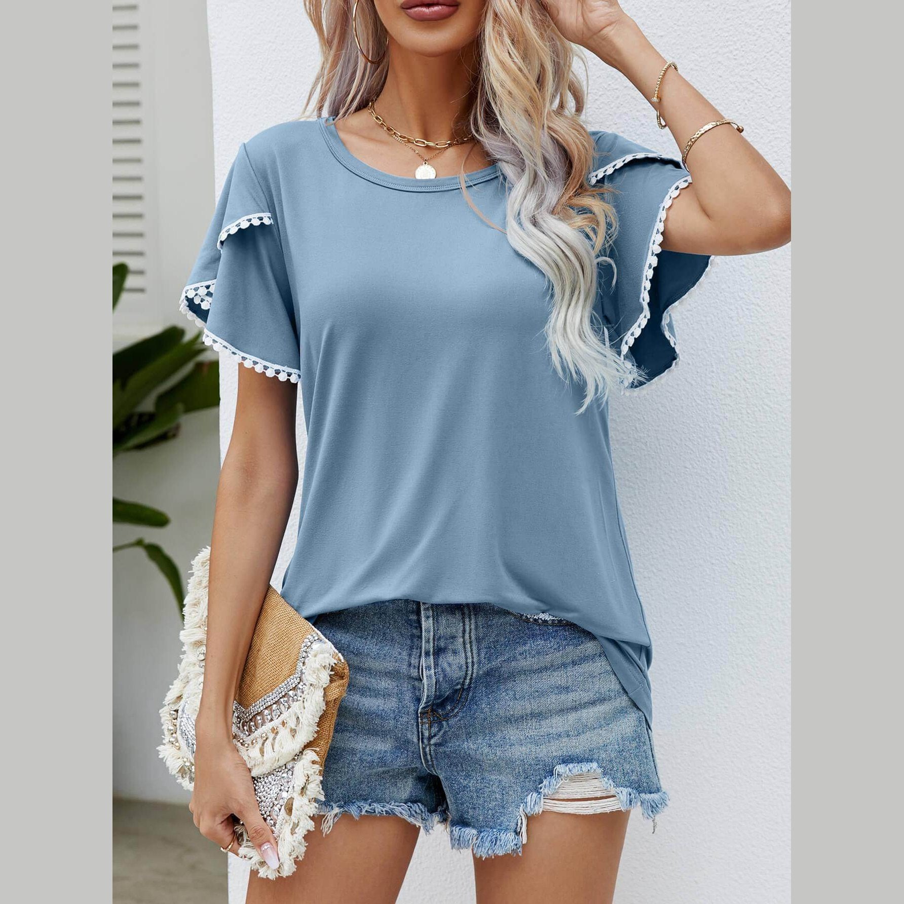 Stylish women's pom-pom flutter sleeve tee in blue, paired with denim shorts for a casual look