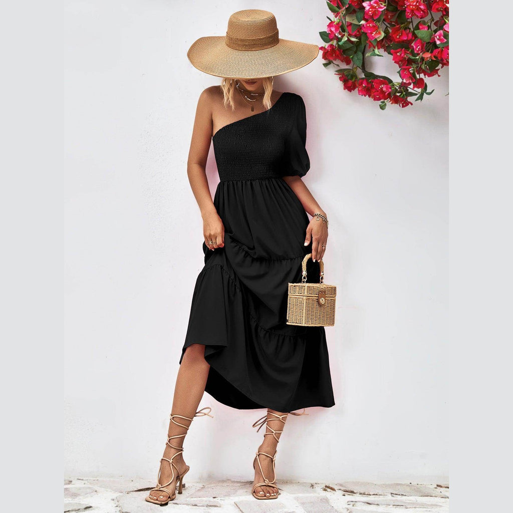 Chic black stylish one-shoulder dress paired with a wide-brimmed hat and a woven handbag