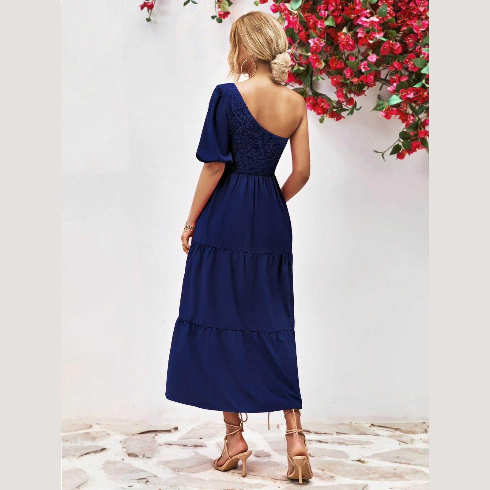 Back view of a navy stylish one-shoulder dress with puff sleeves and tiered design